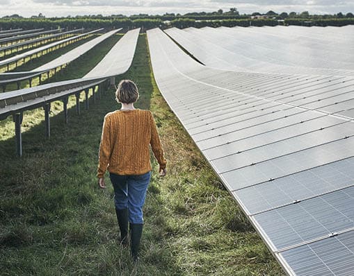 Young female farmer walking away from camera, between solar panels on her solar farm