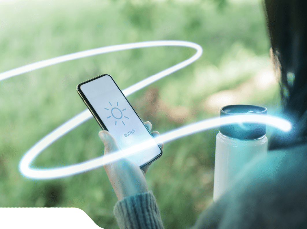 Over the shoulder view of a woman looking at weather forecast using mobile app on smartphone and holding a travel mug.