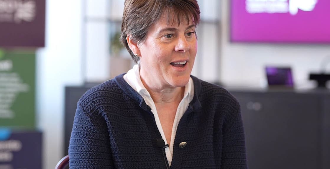 A woman wearing a blue sweater and white shirt. Description generated by AI